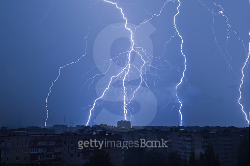 Lightning over the city in the night sky strikes the roof of the house ...