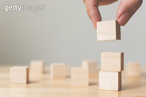 Hand arranging wood block stacking on top with wooden table. Business ...
