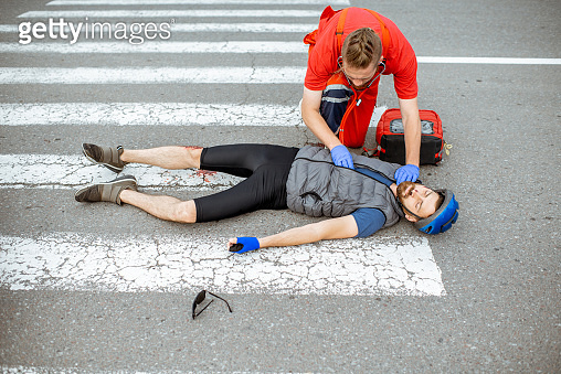 Medic applying first aid to the injured man on the road (1162084054 ...