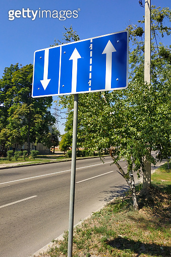 The road sign is blue with white arrows indicating the direction of ...