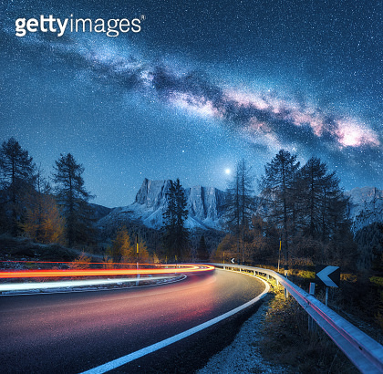 Milky Way over mountain road. Blurred car headlights on winding road in ...