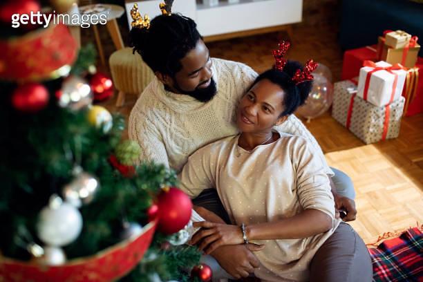 Happy African American couple relaxing by Christmas tree at home ...