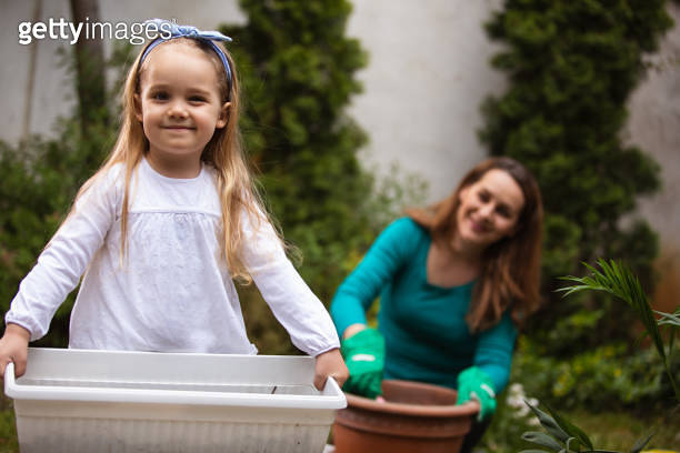 Adorable little girl holding a flower pot and looking at camera ...
