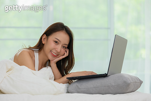 Beautiful Attractive Asian young woman lying on bed and using computer ...
