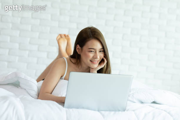 Beautiful Attractive Asian young woman lying on bed and using computer ...