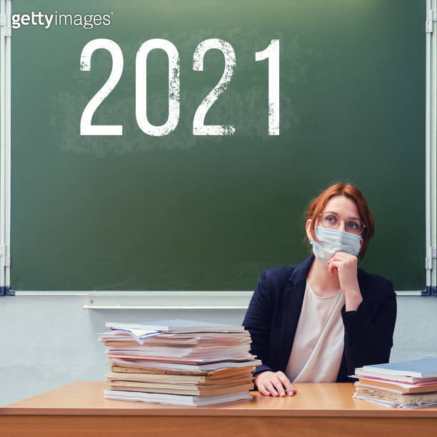 Woman teacher sitting in a medical mask at the blackboard with the ...