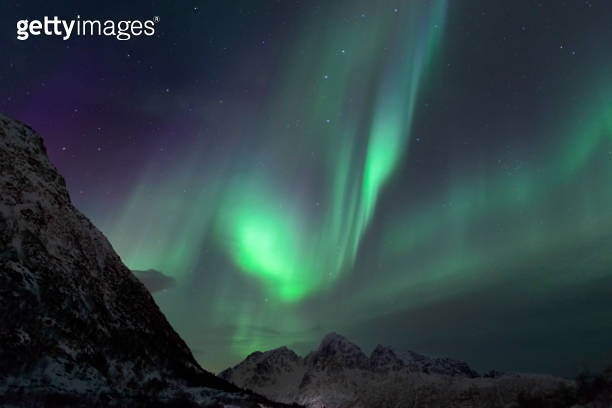 Aurora borealis over in the dark night sky over the snowy mountains in ...
