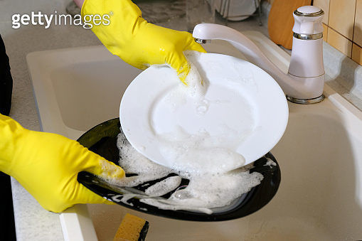 Hands in yellow protective rubber gloves washing dishes in the kitchen ...