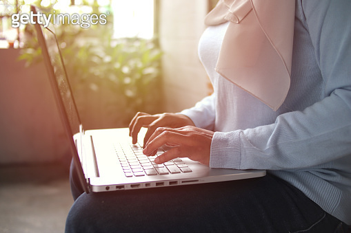 Asian muslim woman wearing hijab smiling while typing on her laptop ...