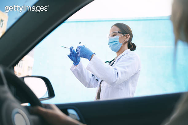 Shot of a masked young doctor giving a patient an injection at a Covid ...