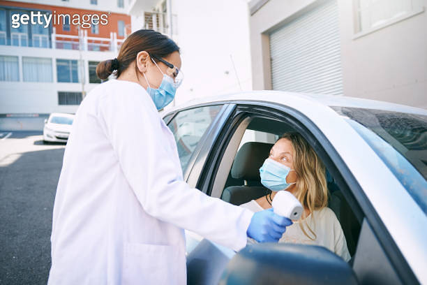 Shot of a masked young woman getting her temperature checked by a ...