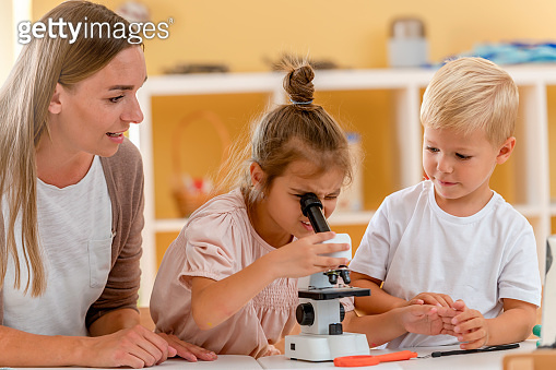 Young children are looking through the microscope while doing a science ...