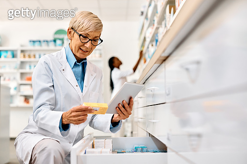 Senior pharmacist using touchpad while going through inventory in a ...