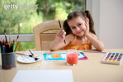 Cheerful little girl sitting at a table and cutely smiling at the ...