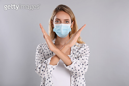 Woman in protective face mask showing stop gesture on grey background ...