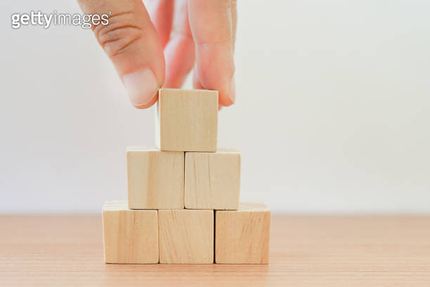 hand arranging wood block stacking as pyramid shape on wooden table for ...