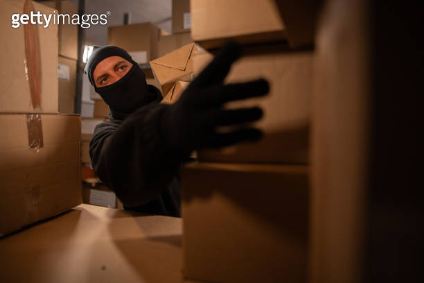 Thief in black balaclava steals with a parcel in a warehouse at the ...