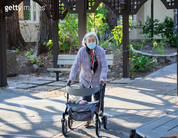 Senior woman with a facemask walking outdoors with her mobility walker ...