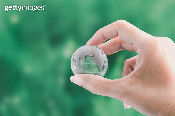 Hands holding globe glass earth with green grass field in side on ...
