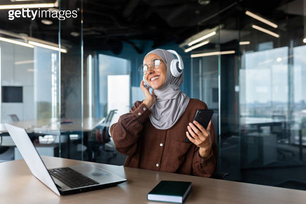 Young Muslim woman in hijab is sitting in the office at the desk and ...