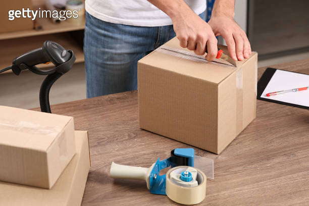 Post office worker with utility knife opening parcel at counter indoors ...