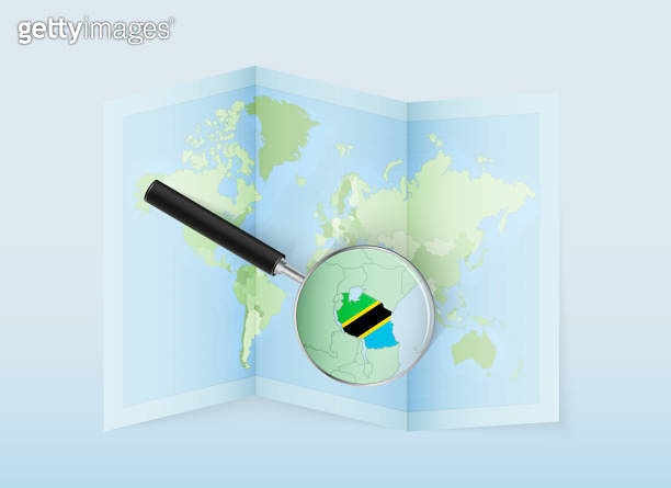 A folded world map with a magnifying lens pointing towards Tanzania ...