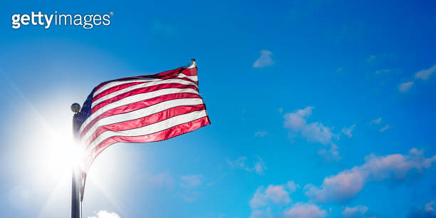 American flag at flagpole over sunny blue sky with shinning sun ...