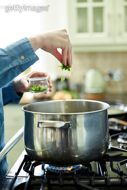 Female hand adding cilantro to cooking pan on stove (478329840) - 게티이미지뱅크