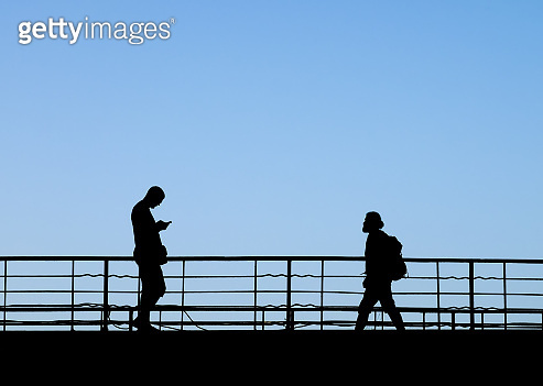 Silhouettes of two people walking towards each other by footbridge 이미지 ...