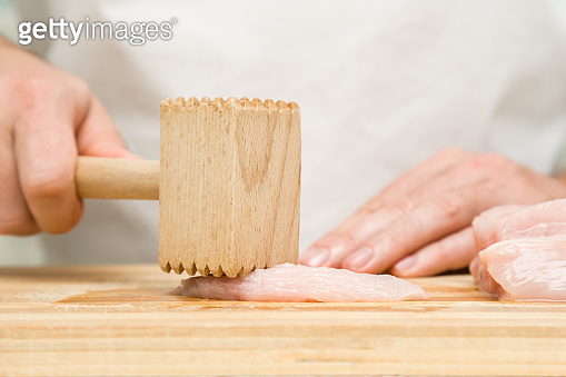 Chef's hands with a wooden hammer beating a chicken meat on the cutting ...