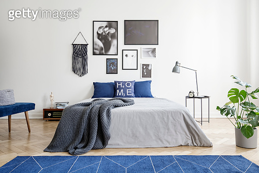 Navy blue carpet in front of grey bed with blanket in bedroom interior ...