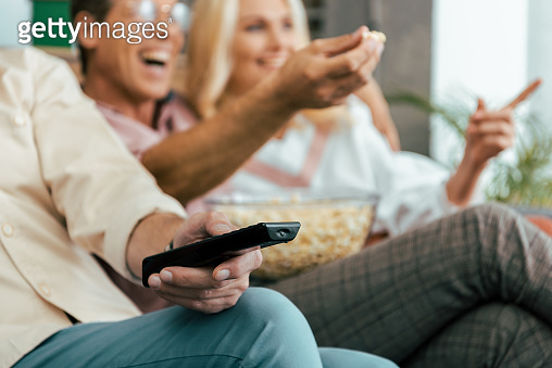 cropped shot of mature friends using remote controller and eating ...