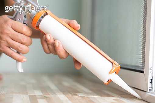 Window Connection Glue Men's hand uses silicone adhesive with a glue gun to repair worn ...