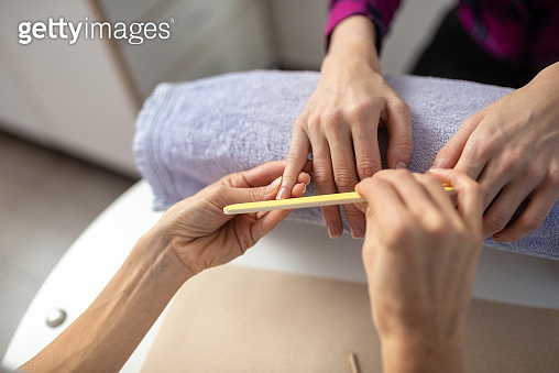 Over the shoulder view of professional manicurist filing nails ...