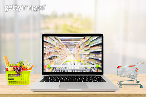 laptop computer and shopping cart on wood table with window curtain ...