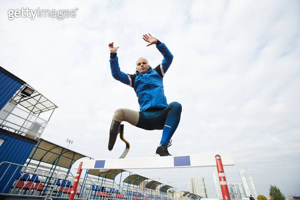 Young active runner with prosthetic curved blade jumping over obstacles ...