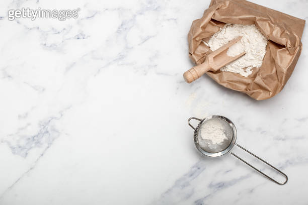 Wheat flour and a wooden scoop in a paper bag on a marble table. bakery