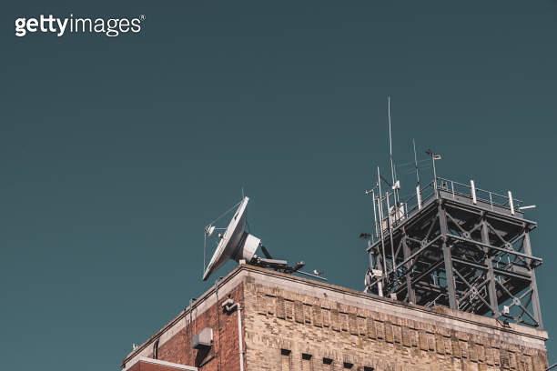Satellite disk and communications tower on the roof of a brick building ...