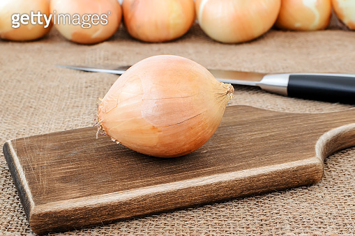 One fresh yellow onion on a brown wooden cutting board and sharp chef ...