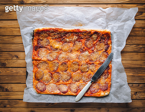Homemade pizza rectangle form with cheese and salami lies on papyrus on ...