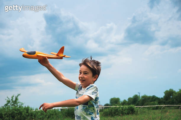 Close-up happy kid playing with toy airplane against stormy summer sky ...