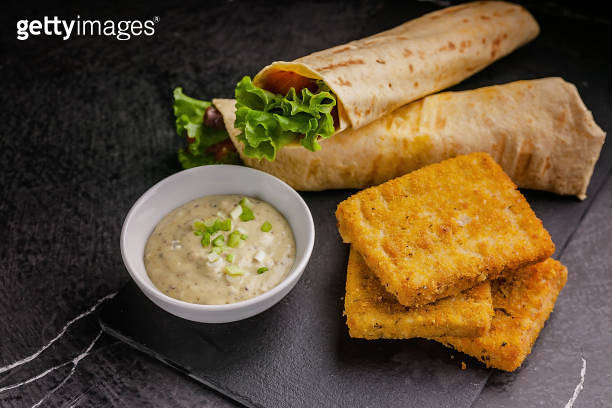 Close up tortilla wrap with salmon and fresh salad, breaded fish fillet ...