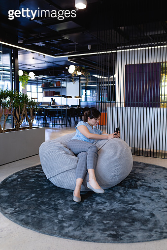 Asian woman using her phone in a bean bag 이미지 (1215729823) - 게티이미지뱅크