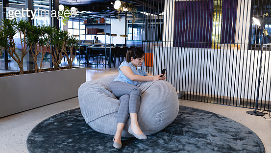 Asian woman using her phone in a bean bag 이미지 (1215729809) - 게티이미지뱅크
