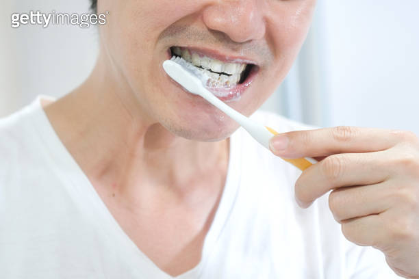 A young Asian man, he cleans his teeth with a brush and toothpaste ...