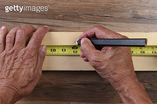 High angle closeup of a carpenters hands using a tape measure to mark a ...