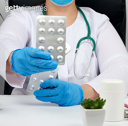 female hand with blue sterile gloves holds a stack of pills in a ...