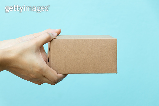 Woman hand hold the brown corrugated box on blue wall background with