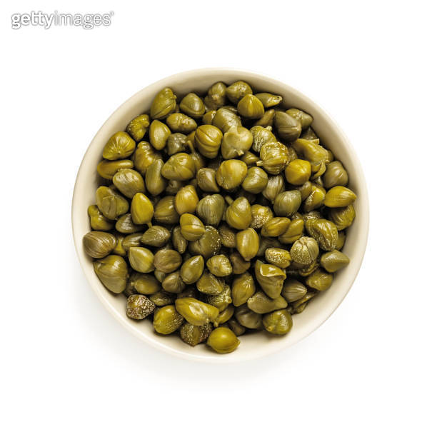 Pickled capers in a beige bowl isolated on white background. Marinated buds of caper bush