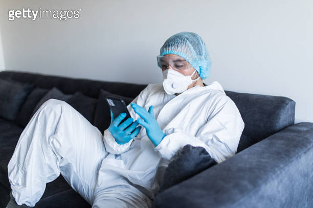 Young man in biohazard clothing using phone and staying at home at self ...